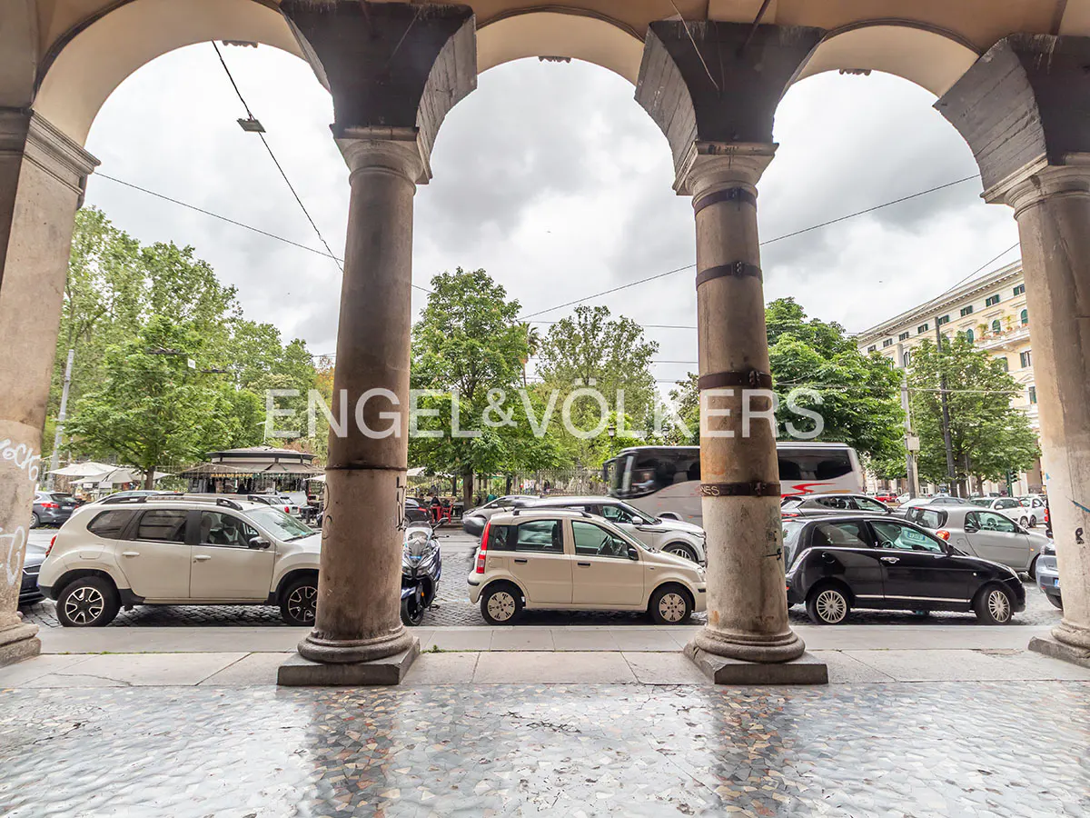 View of street with cars and trees through stone arches. Engel & Volkers logo is superimposed on the image.