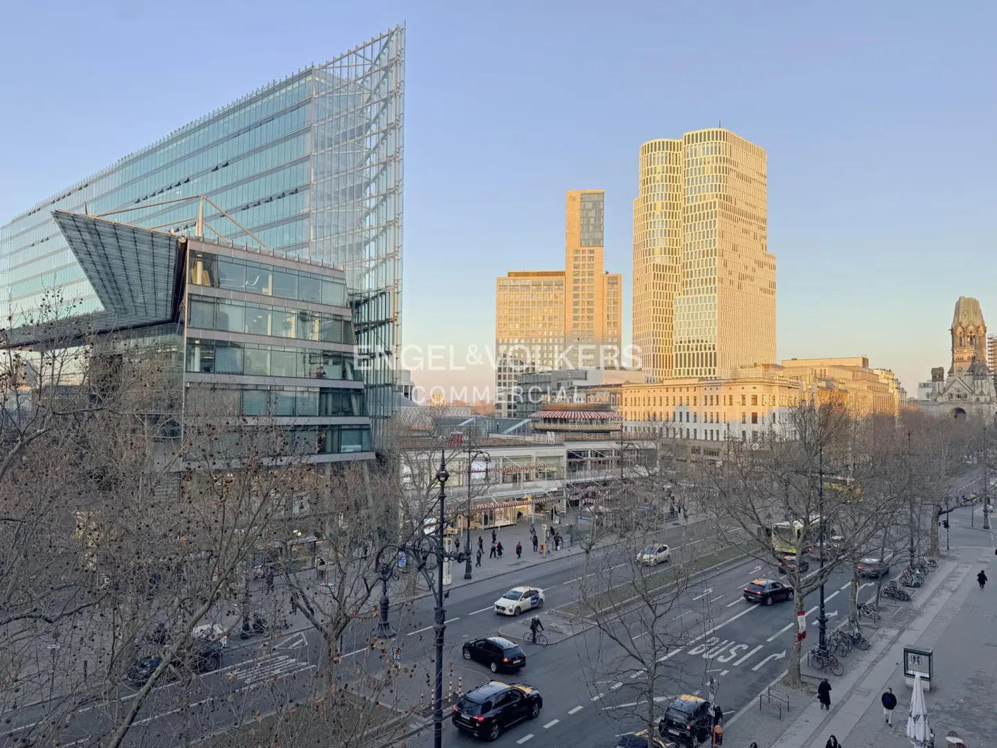 Cityscape view of Berlin, Germany, featuring modern glass buildings, a busy street with cars, and the Kaiser Wilhelm Memorial Church in the background.