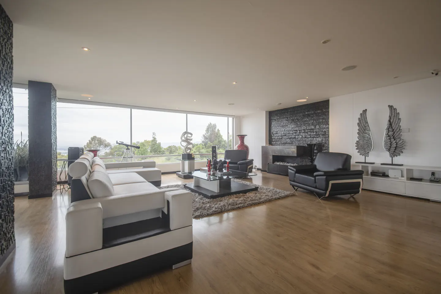 Bright living room with wood floors, a white and black sofa, black leather chairs, and a large window with a view.
