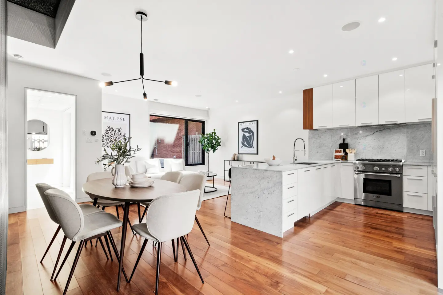 Modern open-concept kitchen and dining area with white cabinets, marble island, and warm hardwood floors.