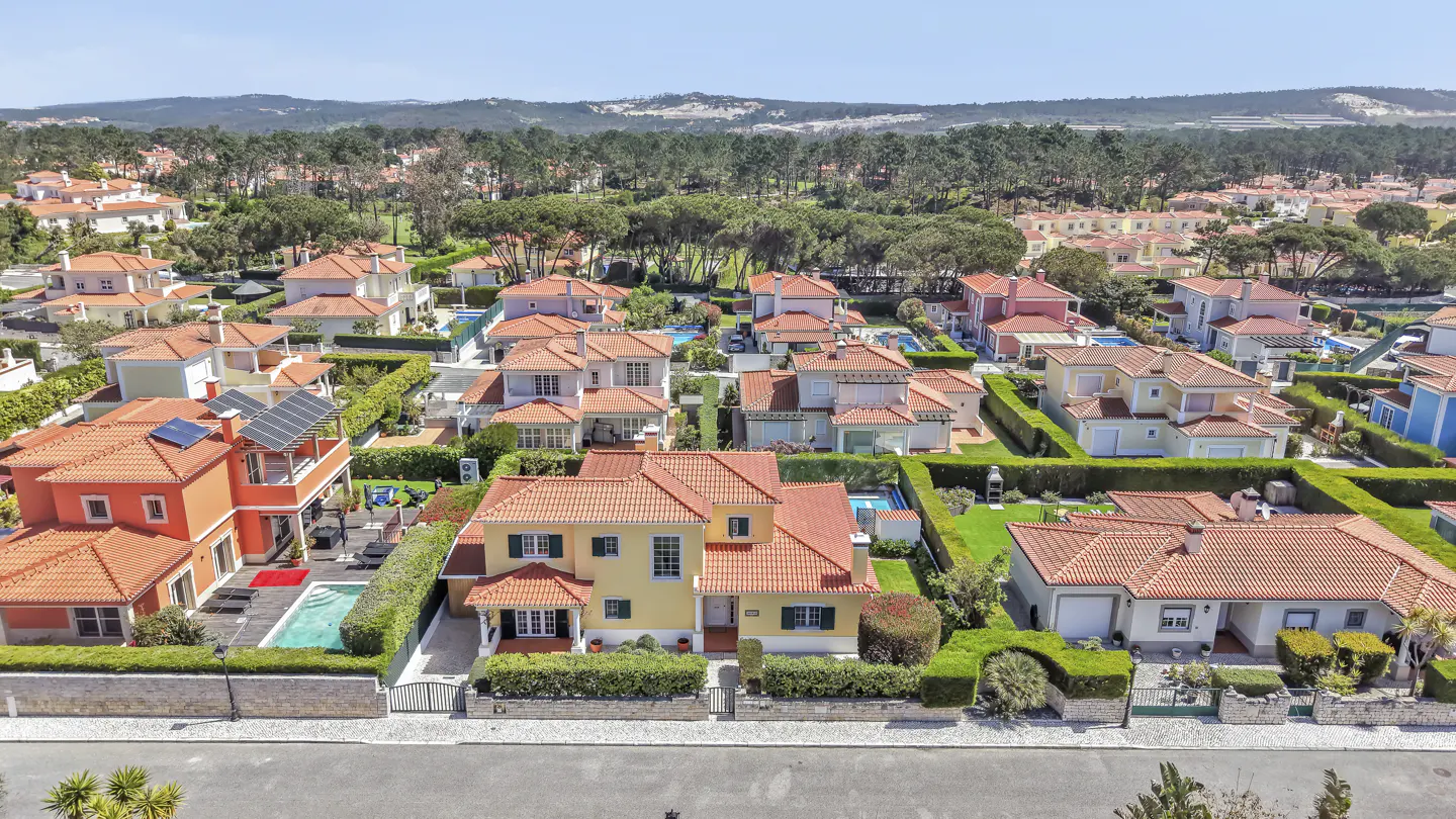Aerial view of a residential neighborhood with houses with orange tile roofs and green trees in the background.