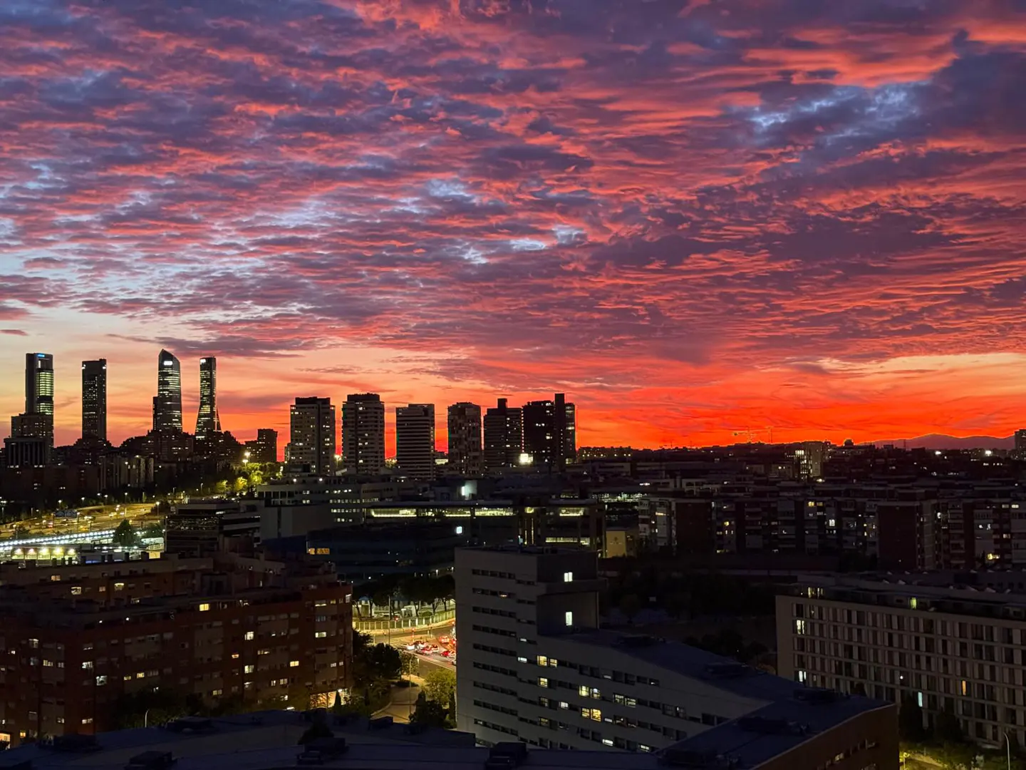 Cityscape view at sunset with tall buildings silhouetted against a vibrant red and purple sky.