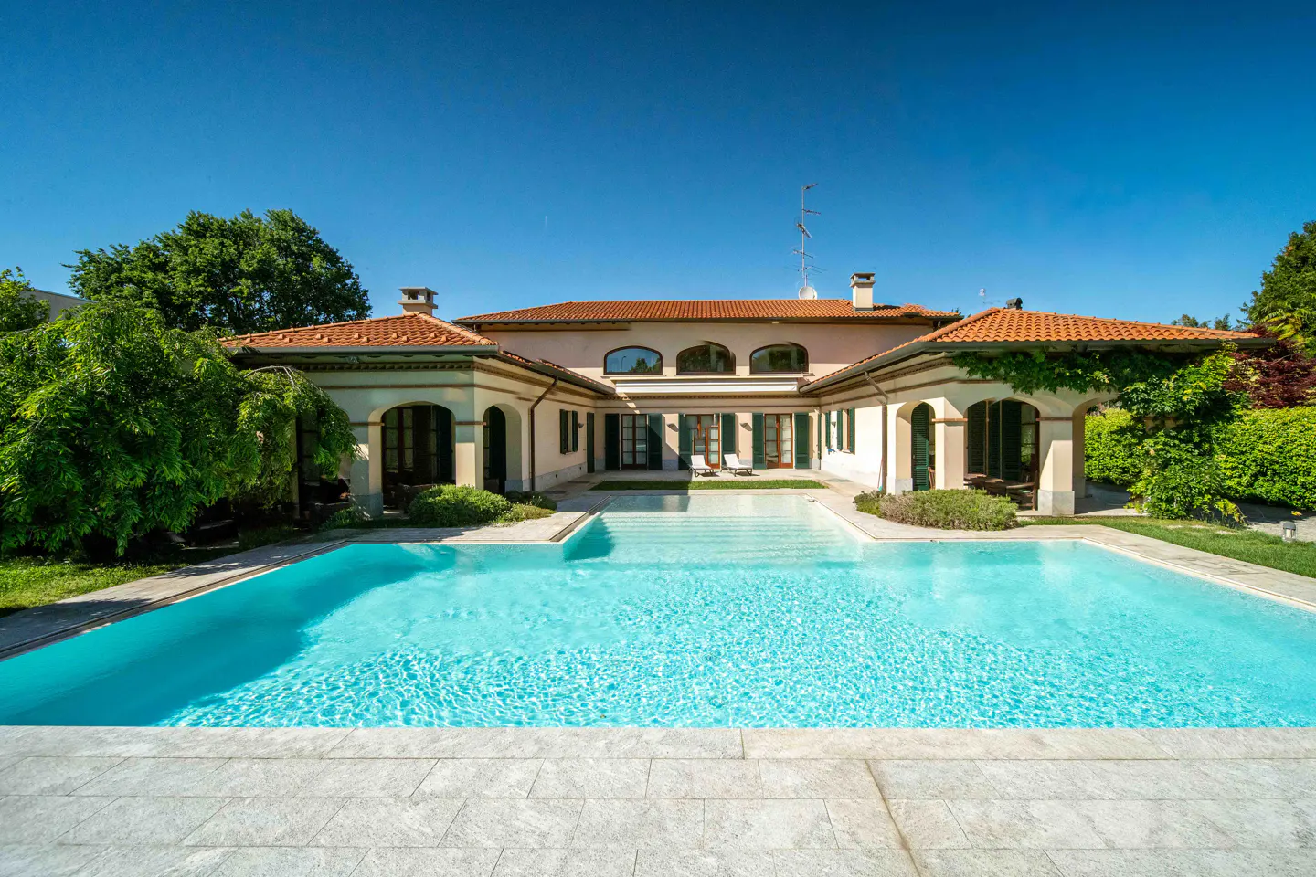 Luxury home with a turquoise pool and a red tile roof under a clear blue sky.