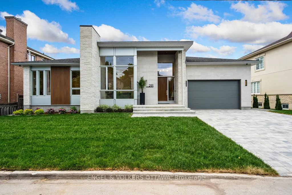 Modern single-story home with a gray garage door, stone facade, and large windows under a cloudy blue sky.