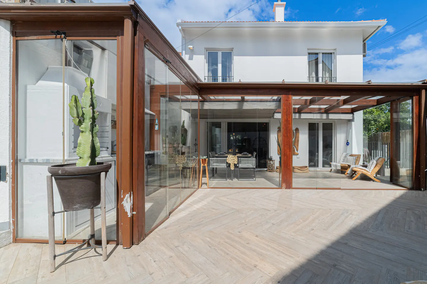 Exterior view of a white two-story house with a glass-enclosed patio and a cactus in a pot.