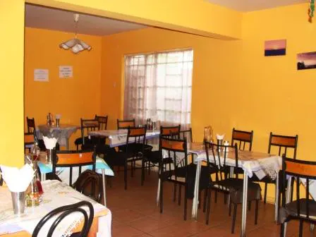 A bright yellow dining room with tables and chairs. A window with white curtains is visible.