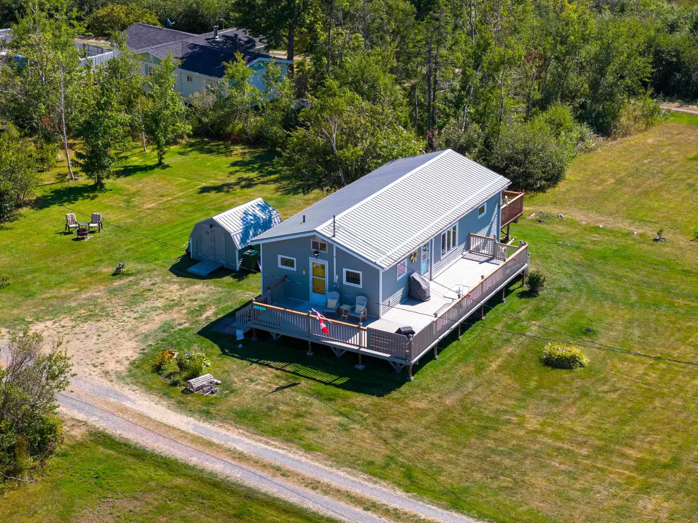 Aerial view of a gray house with a metal roof and a large wooden deck, surrounded by green grass and trees.