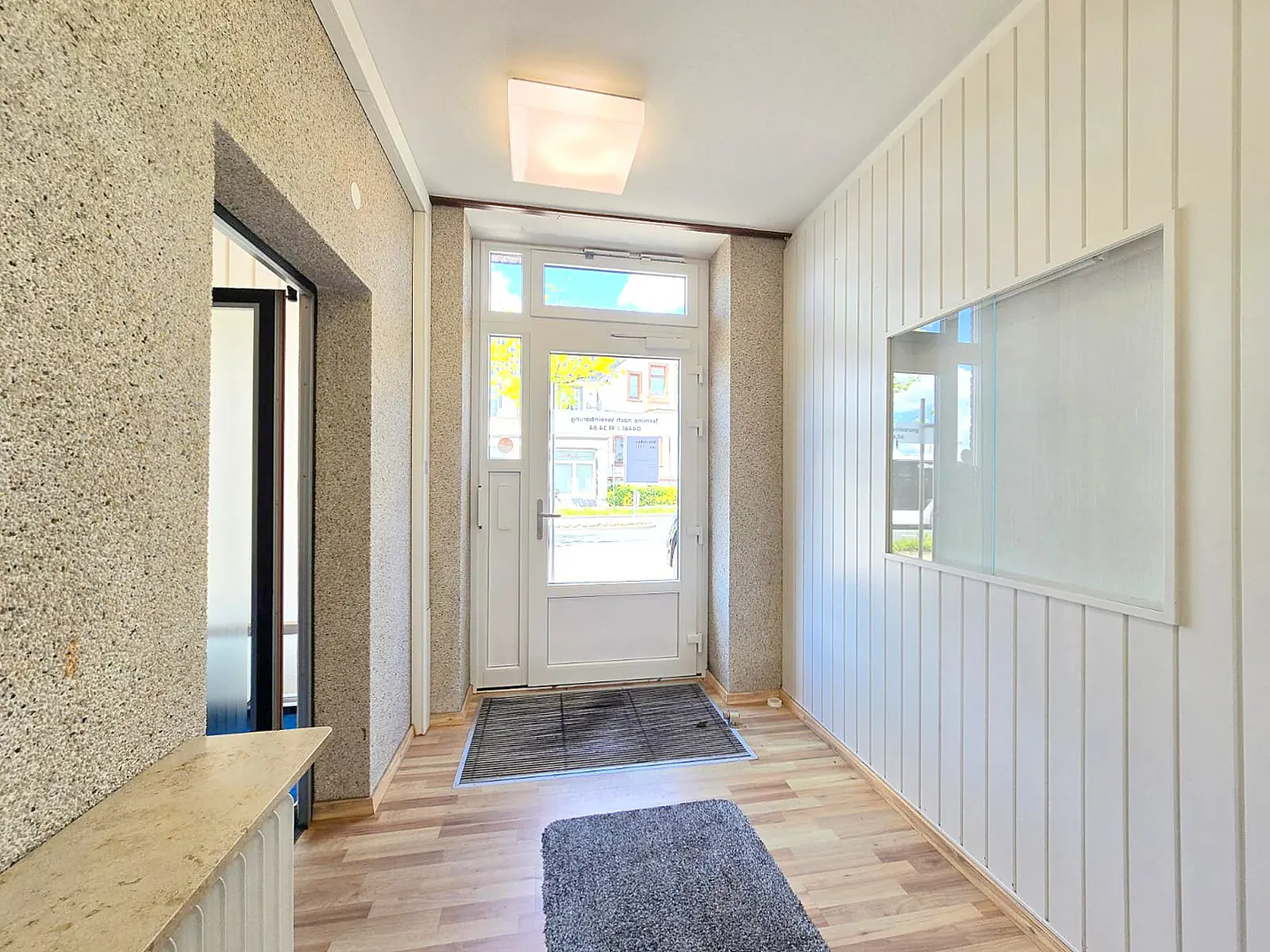 Entryway with wood-look floors, textured walls, and a white front door. A gray rug sits on the floor. A white-framed mirror hangs on the right wall.