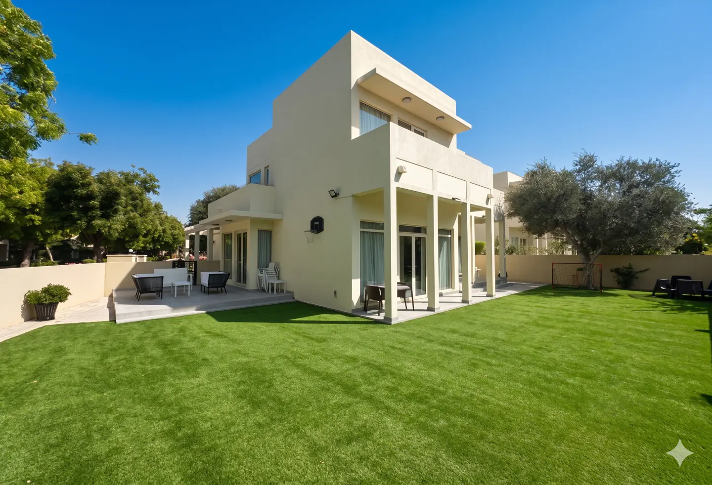 Modern two-story beige villa with a spacious green lawn, patio furniture, and clear blue sky.