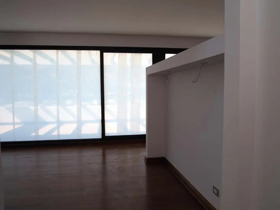 An empty room with hardwood floors, white walls, and a large window with white shades.