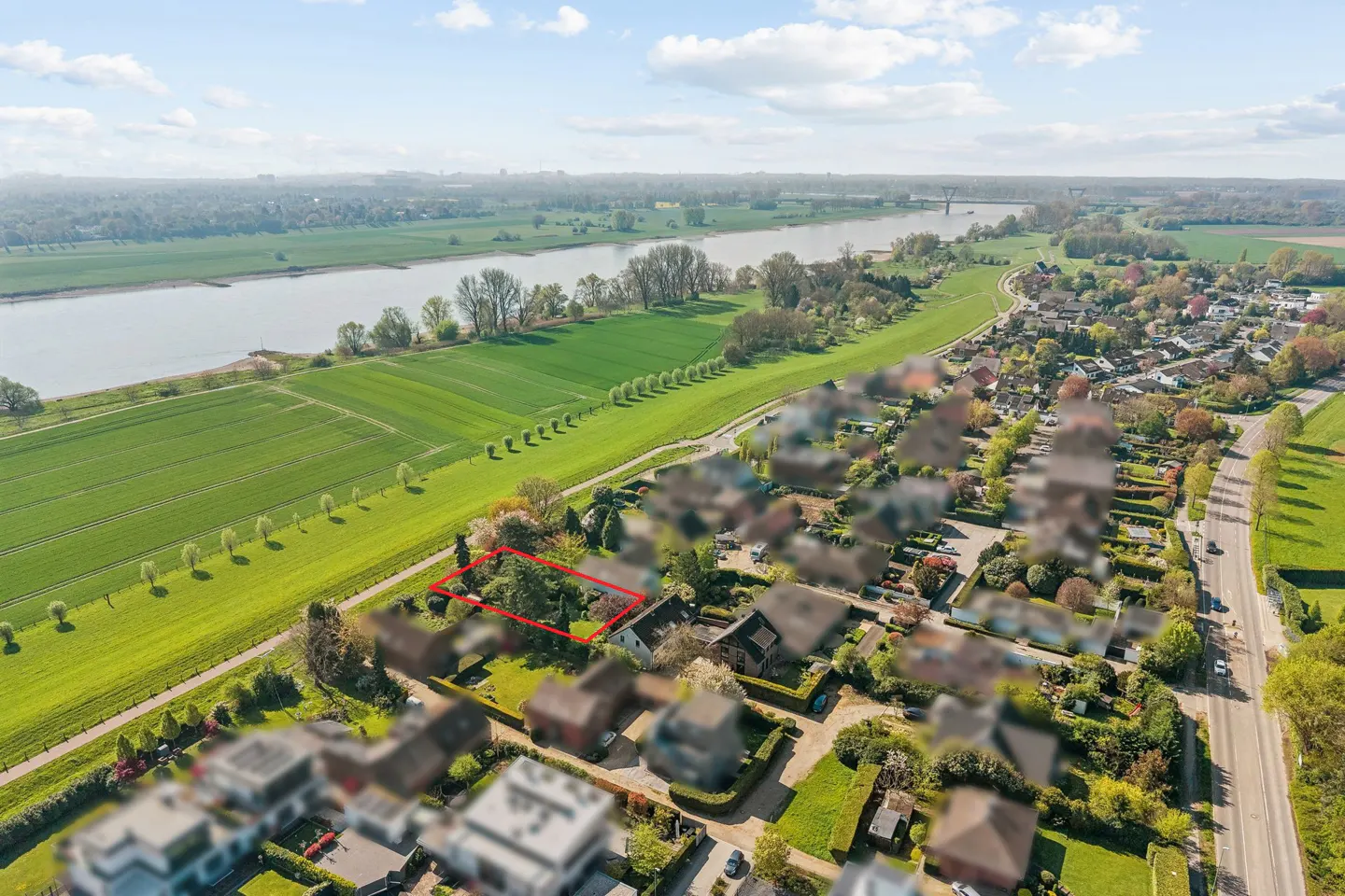 Aerial view of a house with a red border, near a river, green fields, and a residential area.
