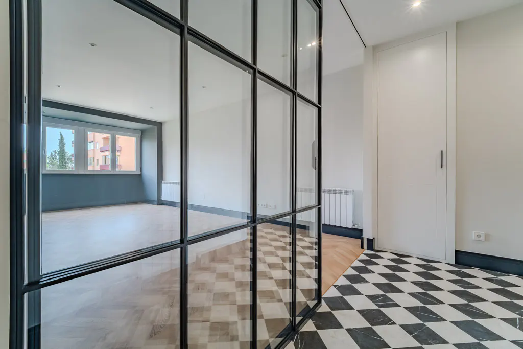 Interior view of a room with a black-framed glass partition, black and white checkered floor, and a white door.