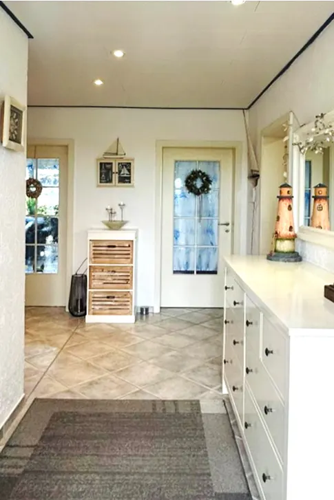 A bright hallway with white walls, tiled floors, and nautical decor. A white dresser with black knobs sits to the right.