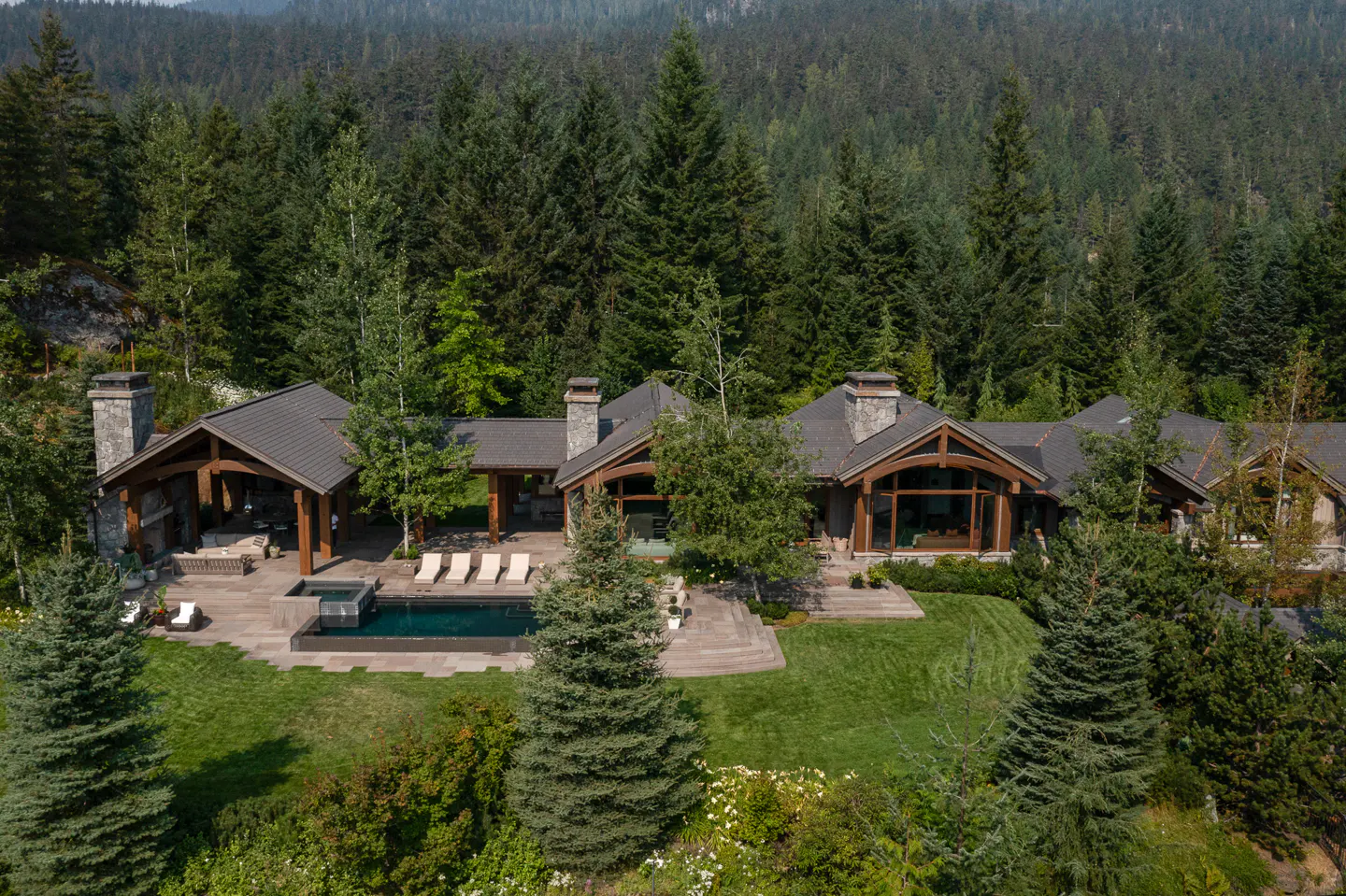 Aerial view of a luxury home with a pool, surrounded by lush green trees and a forest backdrop.