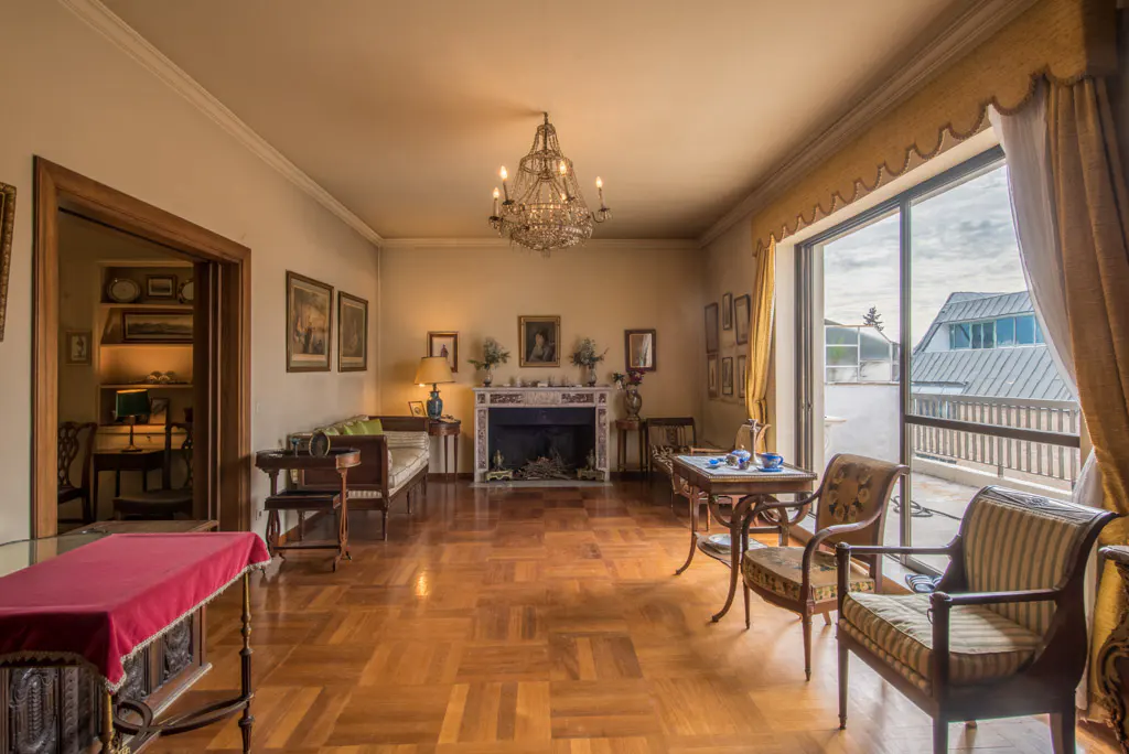 Elegant living room with hardwood floors, fireplace, chandelier, and balcony access. Neutral walls and classic furniture create a sophisticated ambiance.