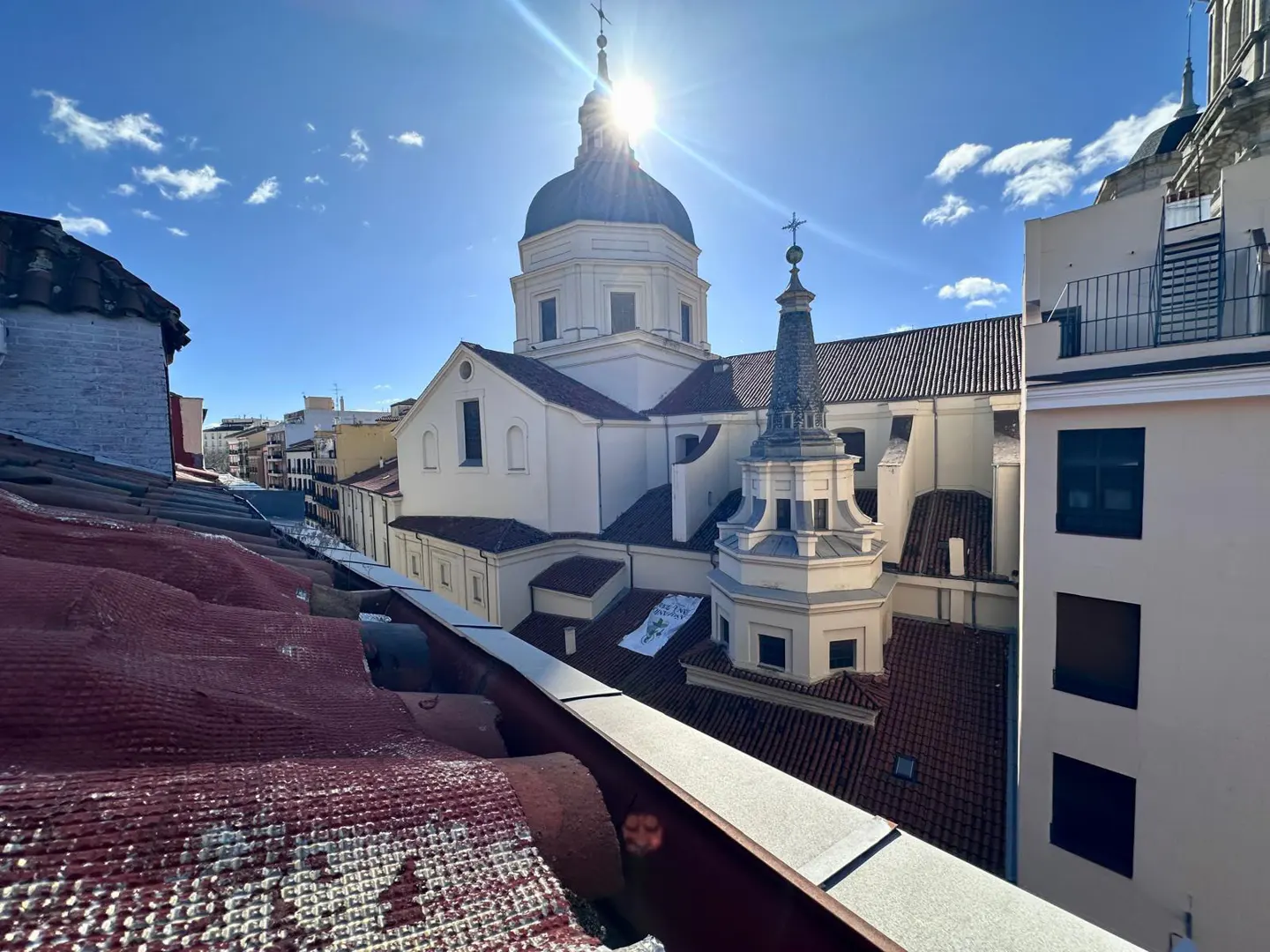 View from a rooftop overlooking a historic white church with a dome and steeple under a bright, sunny blue sky.