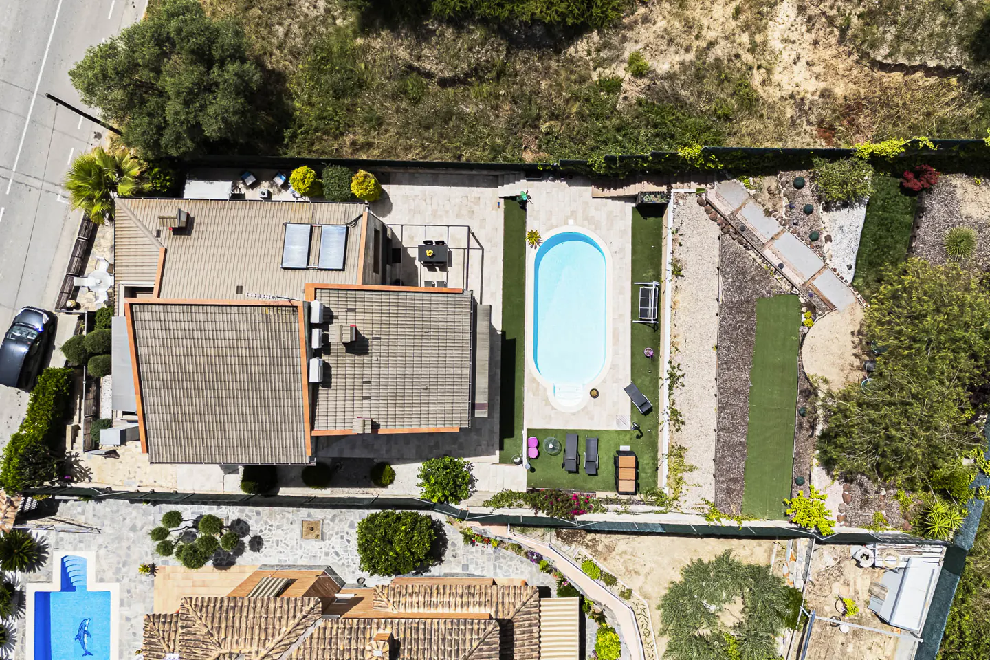 Aerial view of a house with a tiled roof, a rectangular swimming pool, patio furniture, and landscaped garden areas.