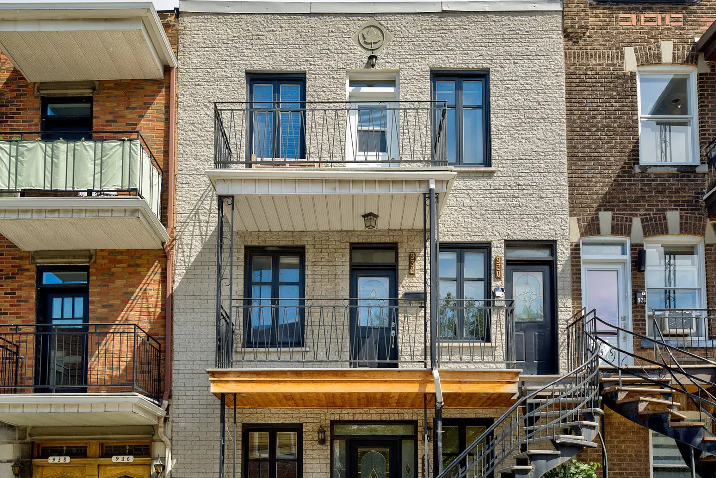 Three-story townhouse with light gray brick, black window frames, two balconies, and a black metal spiral staircase.