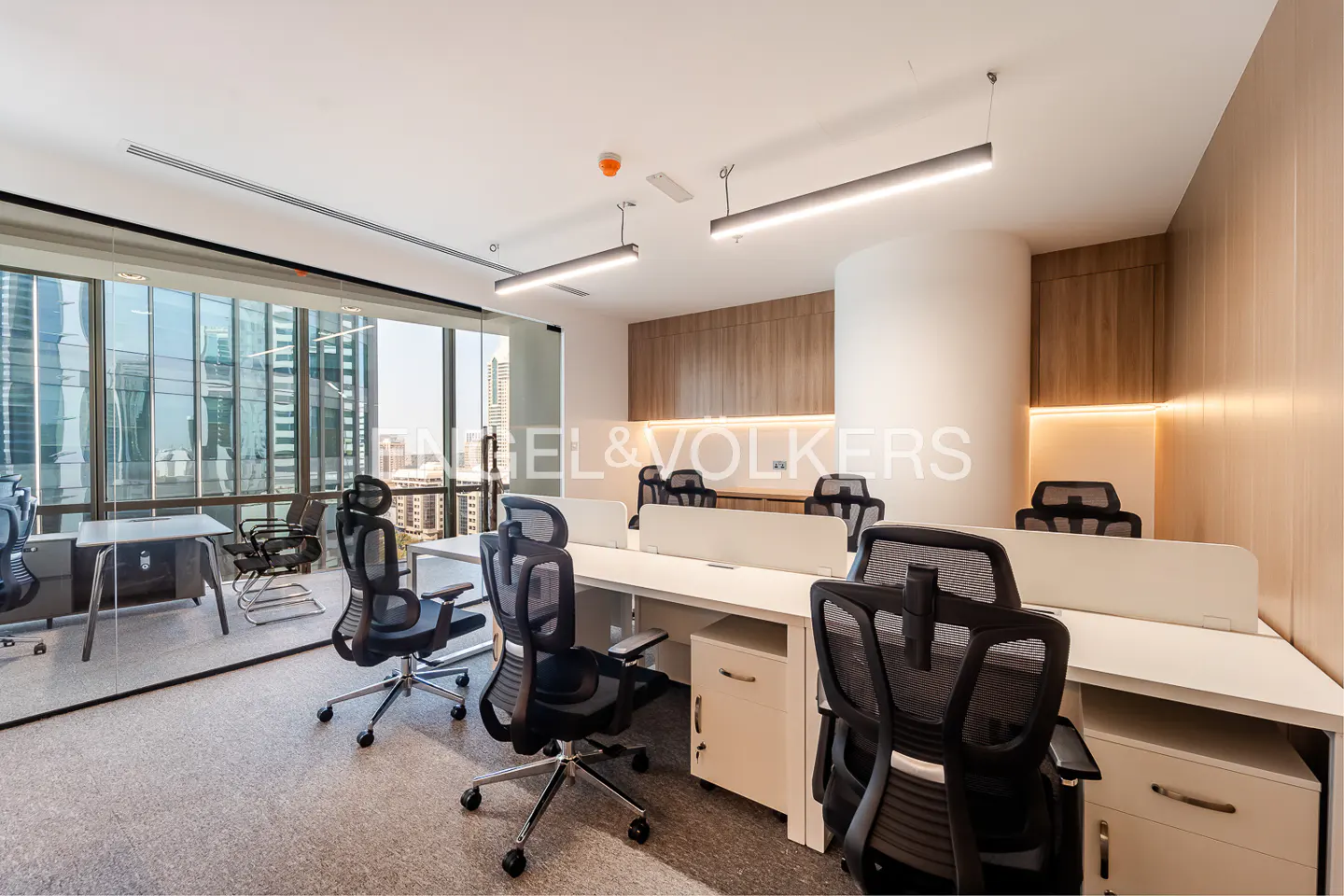 Bright office space with white desks, black mesh chairs, and large windows overlooking a city skyline.