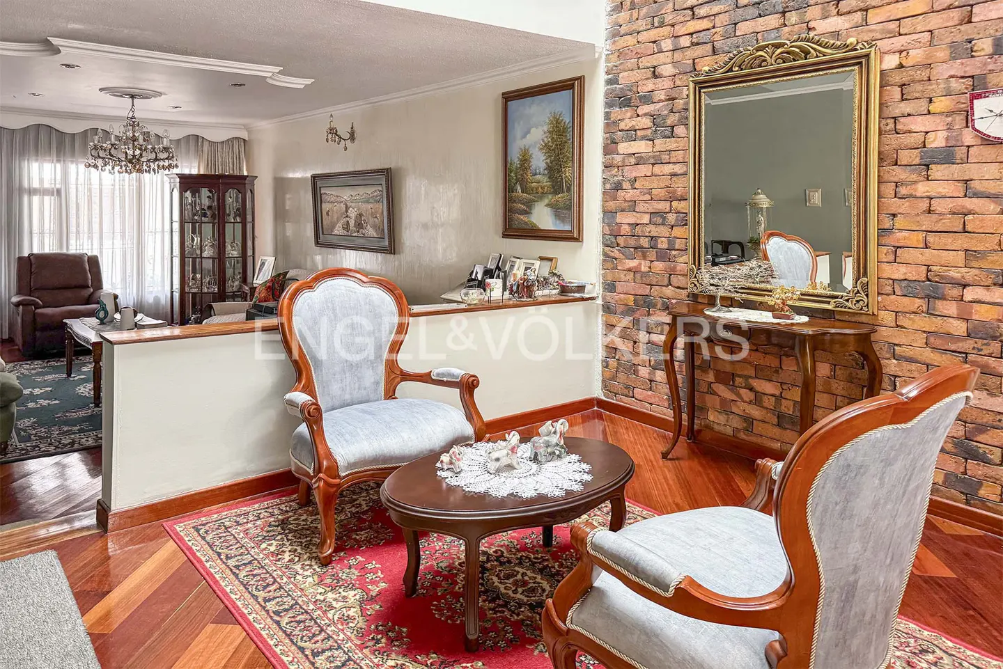 Living room with hardwood floors, brick accent wall, and two light blue armchairs around a dark wood coffee table.