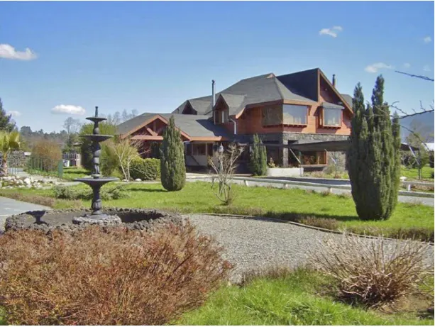 A two-story house with a dark roof and a fountain in the front yard on a sunny day.
