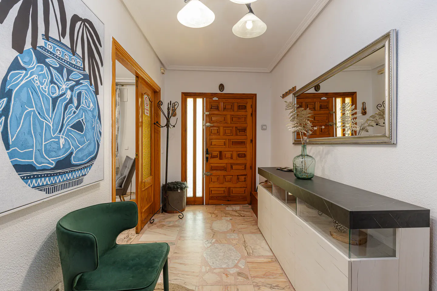 Hallway with a green chair, a blue painting, a wooden door, and a console table with a mirror.