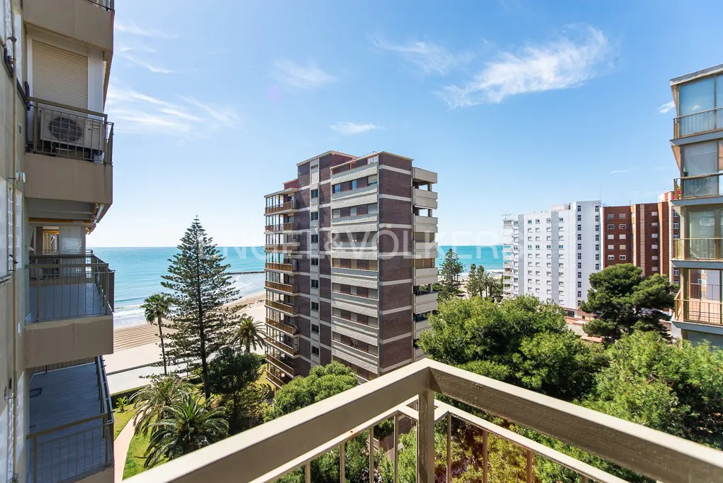 View from a balcony overlooking a beach with tall buildings, trees, and blue sky.
