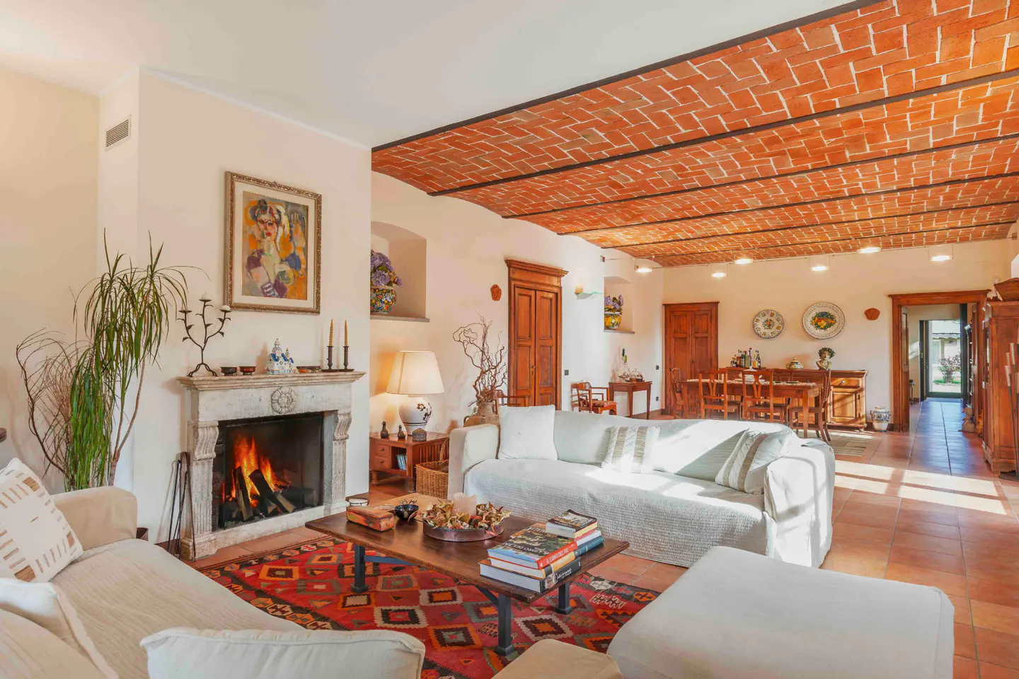 Living room with brick ceiling, fireplace, and white sofas. A red patterned rug sits under a wooden coffee table with books.