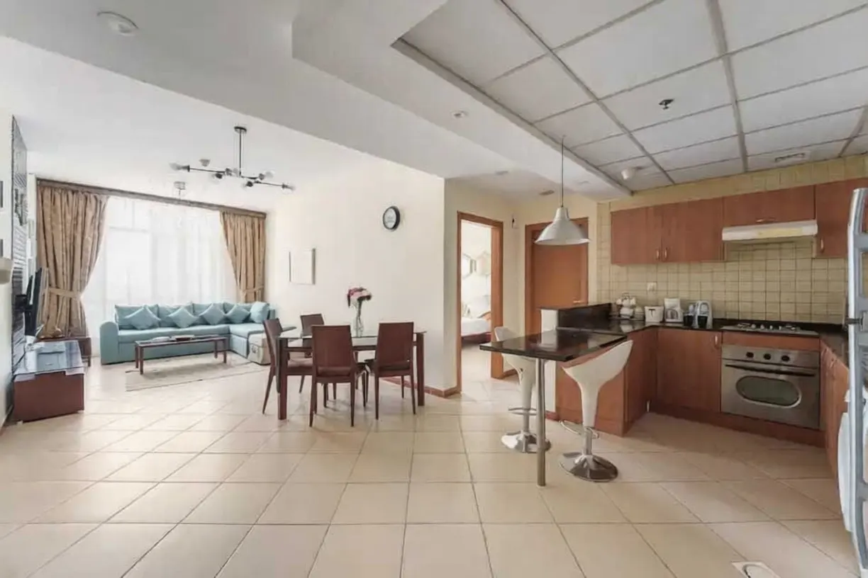 Open-concept apartment with a living room, dining area, and kitchen. A blue sofa sits near a window with tan curtains.