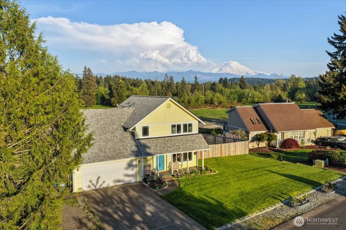 Aerial view of a yellow house with a blue door, green lawn, and mountains in the background.
