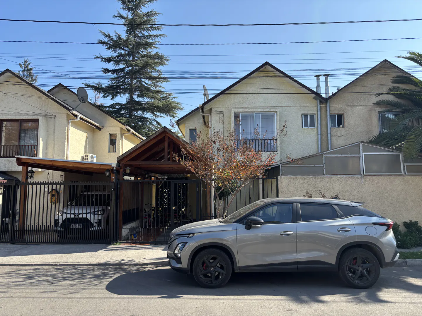 Street view of beige houses with peaked roofs and a silver car parked in front on a sunny day.