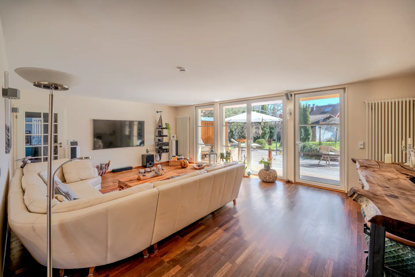 Spacious living room with a cream sectional sofa, wooden floors, wall-mounted TV, and glass doors leading to a patio.