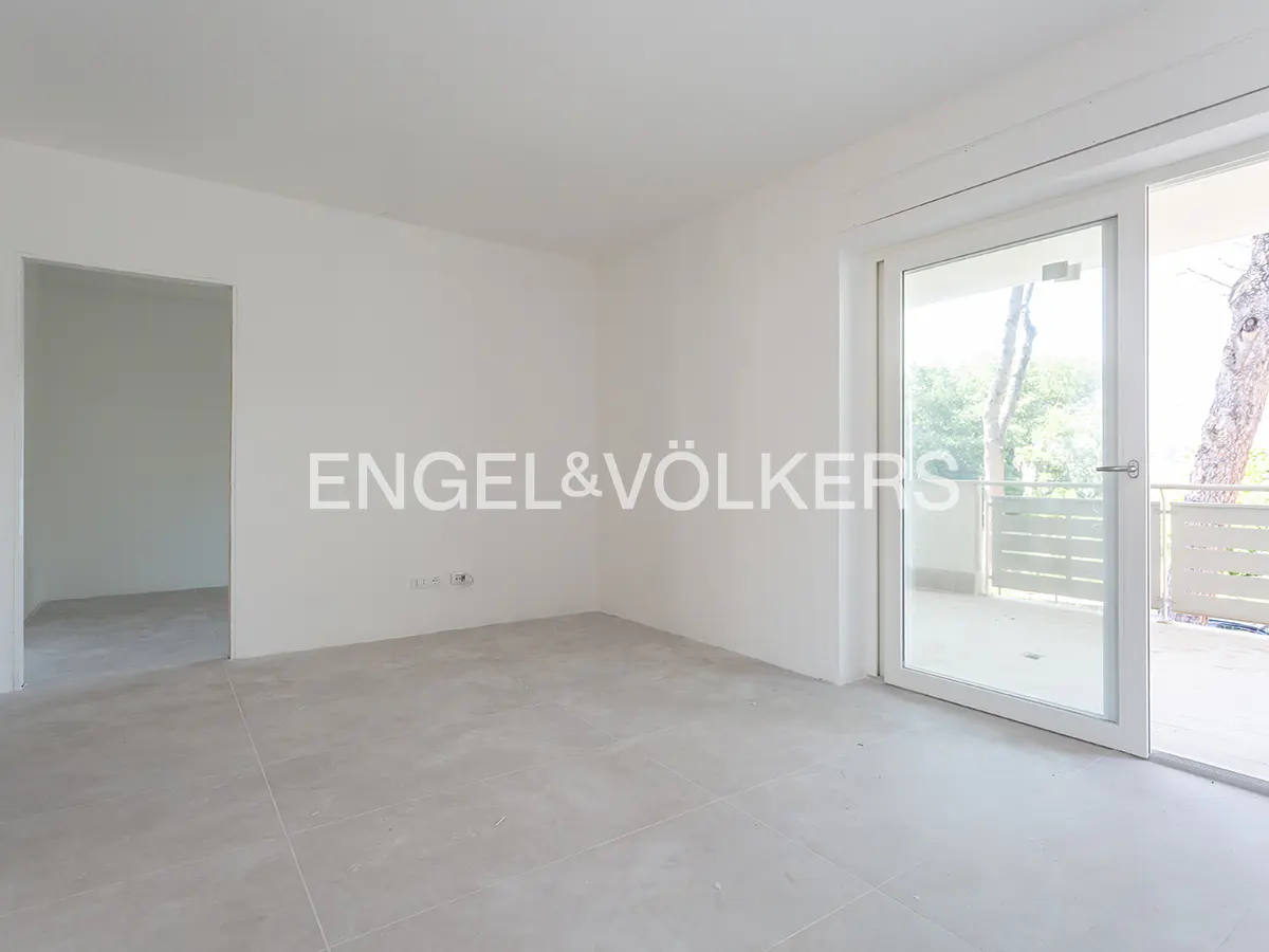Empty room with white walls, light grey tiled floor, a doorway to another room, and a glass door leading to a balcony.