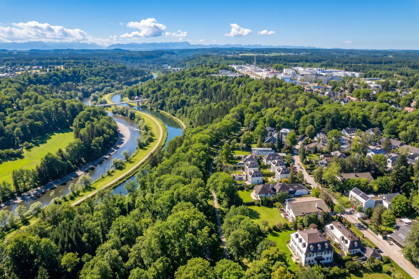 Aerial view of a river winding through a green forest, with houses nestled among the trees and mountains in the distance.