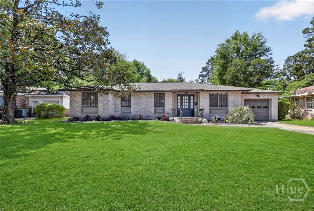 Front exterior of a single-story brick home with a green lawn and a dark blue front door.