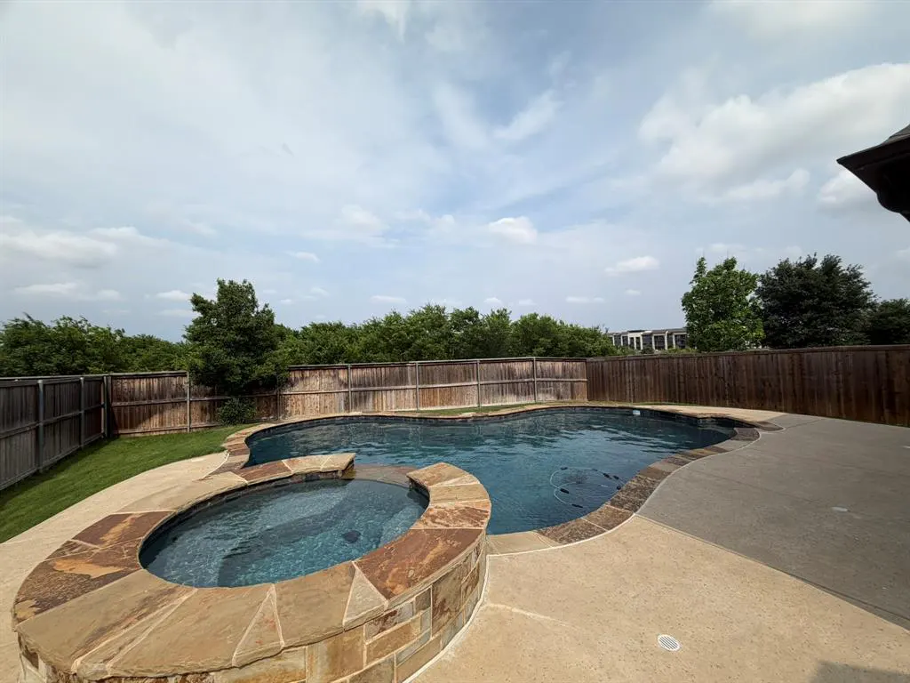 Backyard with a dark blue swimming pool and hot tub, surrounded by a stone deck and a wooden fence.