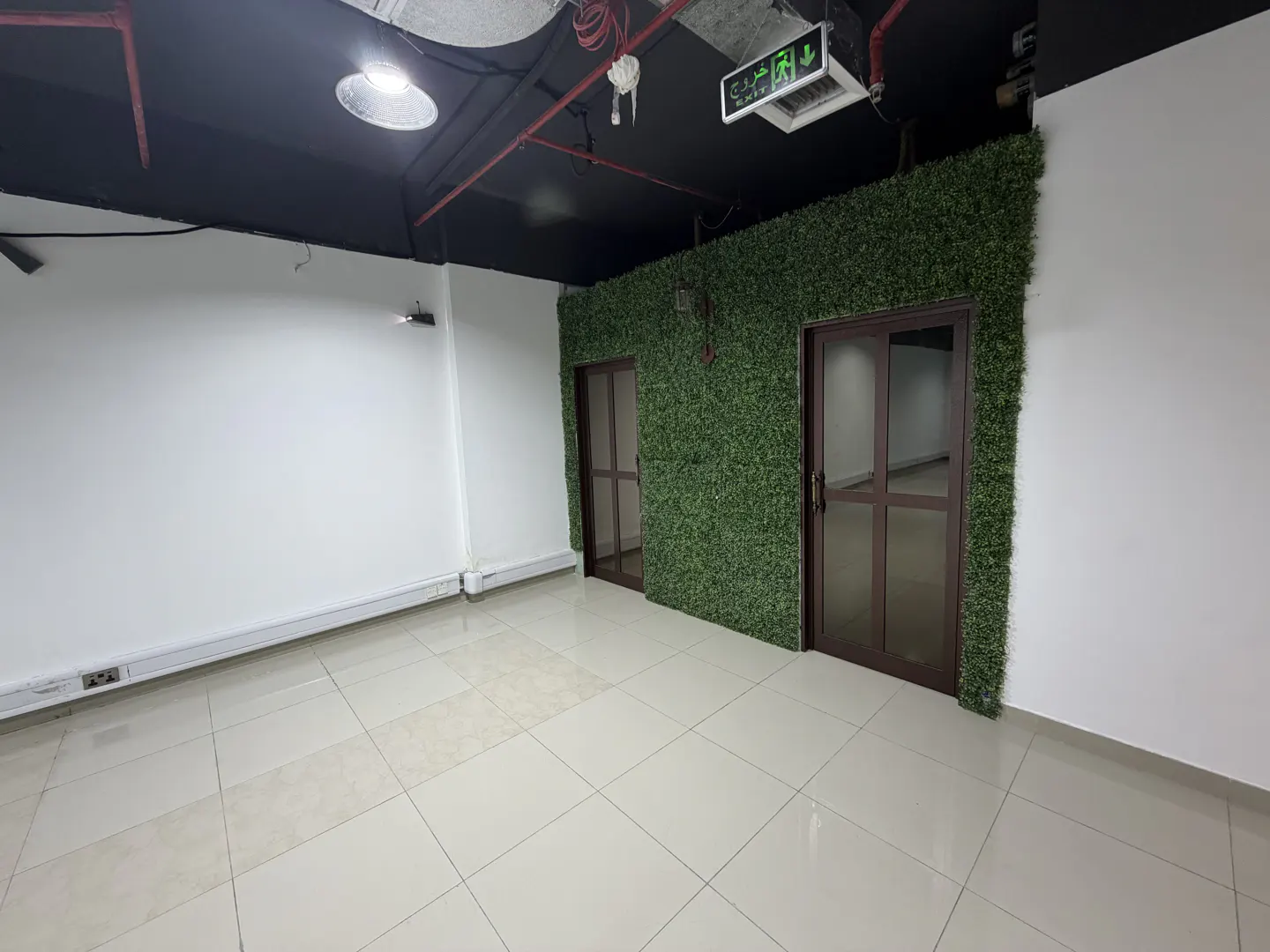 An empty office space with white walls, a black ceiling, and tiled floors. Two doors are framed by a green wall.