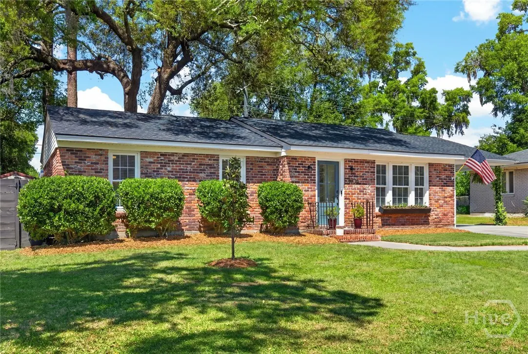 Exterior view of a one-story brick house with a blue door, green lawn, and an American flag.
