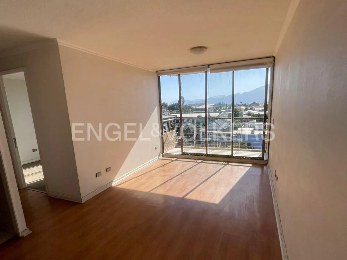 Bright, empty room with wood floors, white walls, and a large window with a view of a city and mountains. Engel & Volkers logo on wall.
