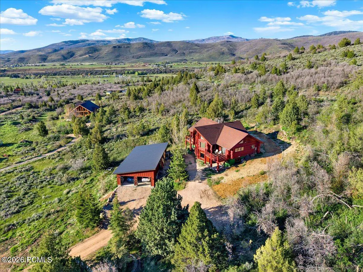 A landscape view of a red log cabin with a garage, surrounded by trees and mountains.
