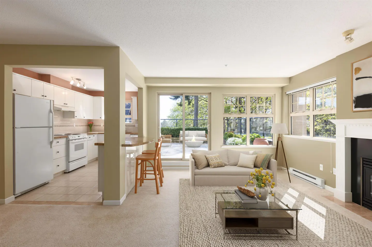 Open-concept living space with a white kitchen, bar stools, and a beige sofa facing a glass coffee table. Sliding doors lead to a patio.