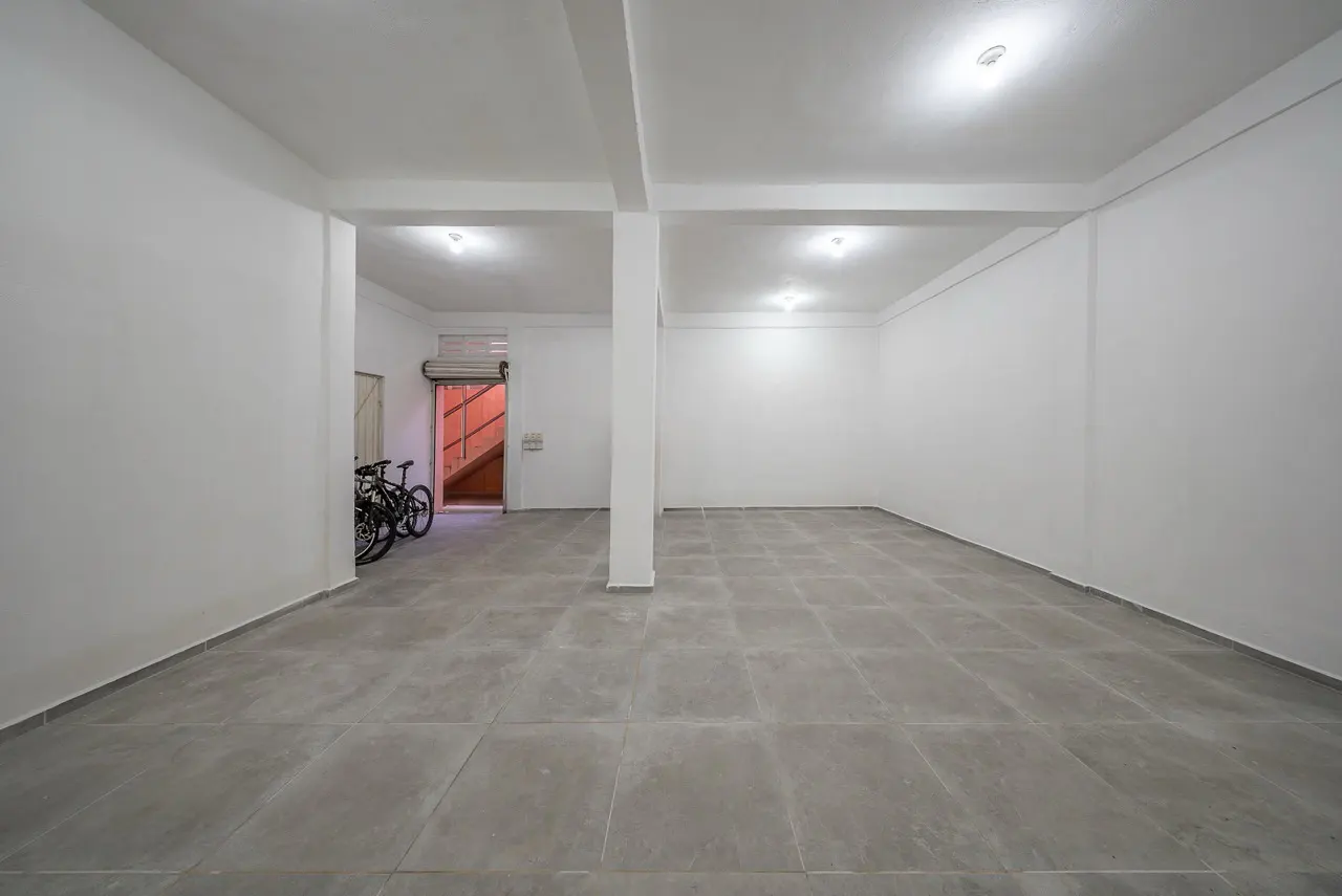 Empty white room with gray tile floor, support beams, and two bicycles near an open door with orange stairs.