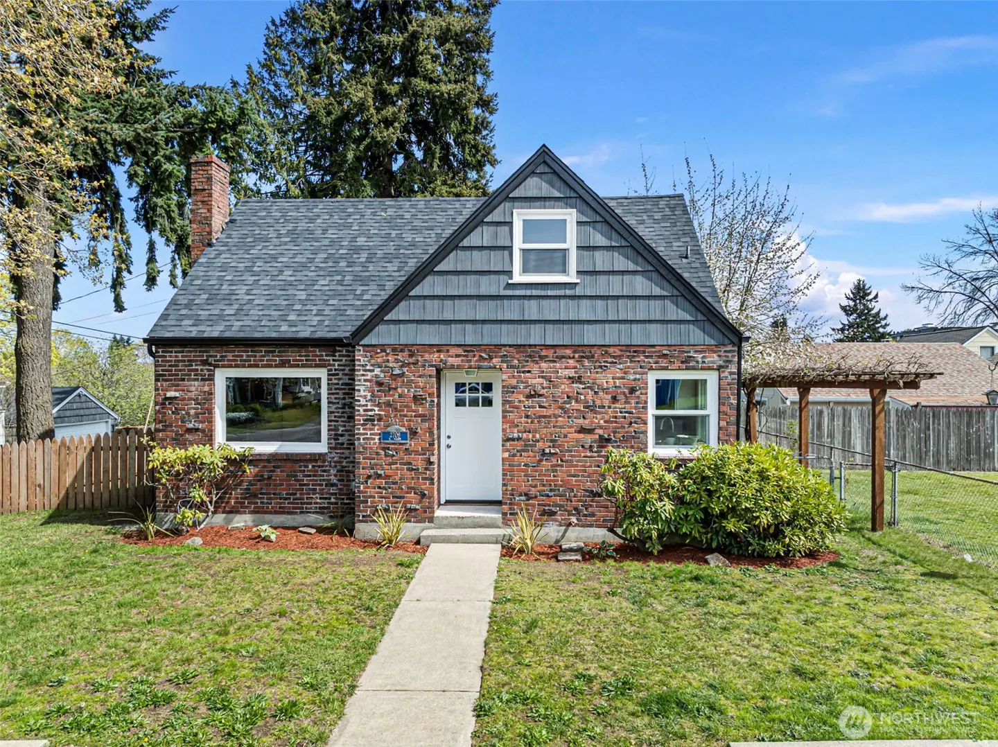 A red brick house with a white door, gray roof, and green lawn on a sunny day.