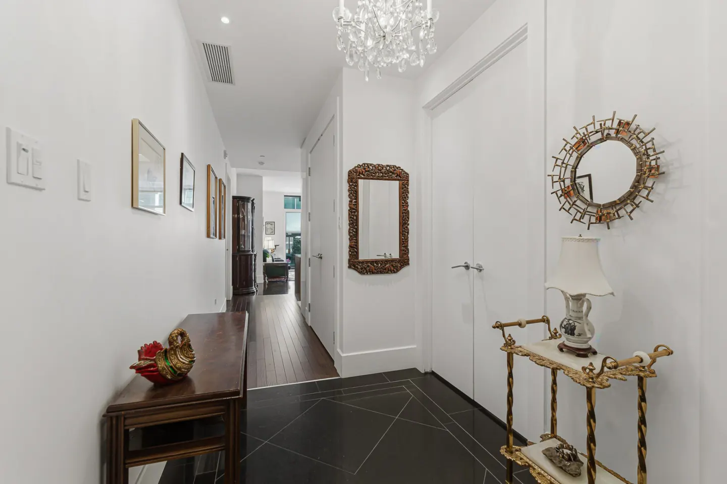 Hallway with black tile floor, white walls, and dark wood furniture. A chandelier hangs from the ceiling.