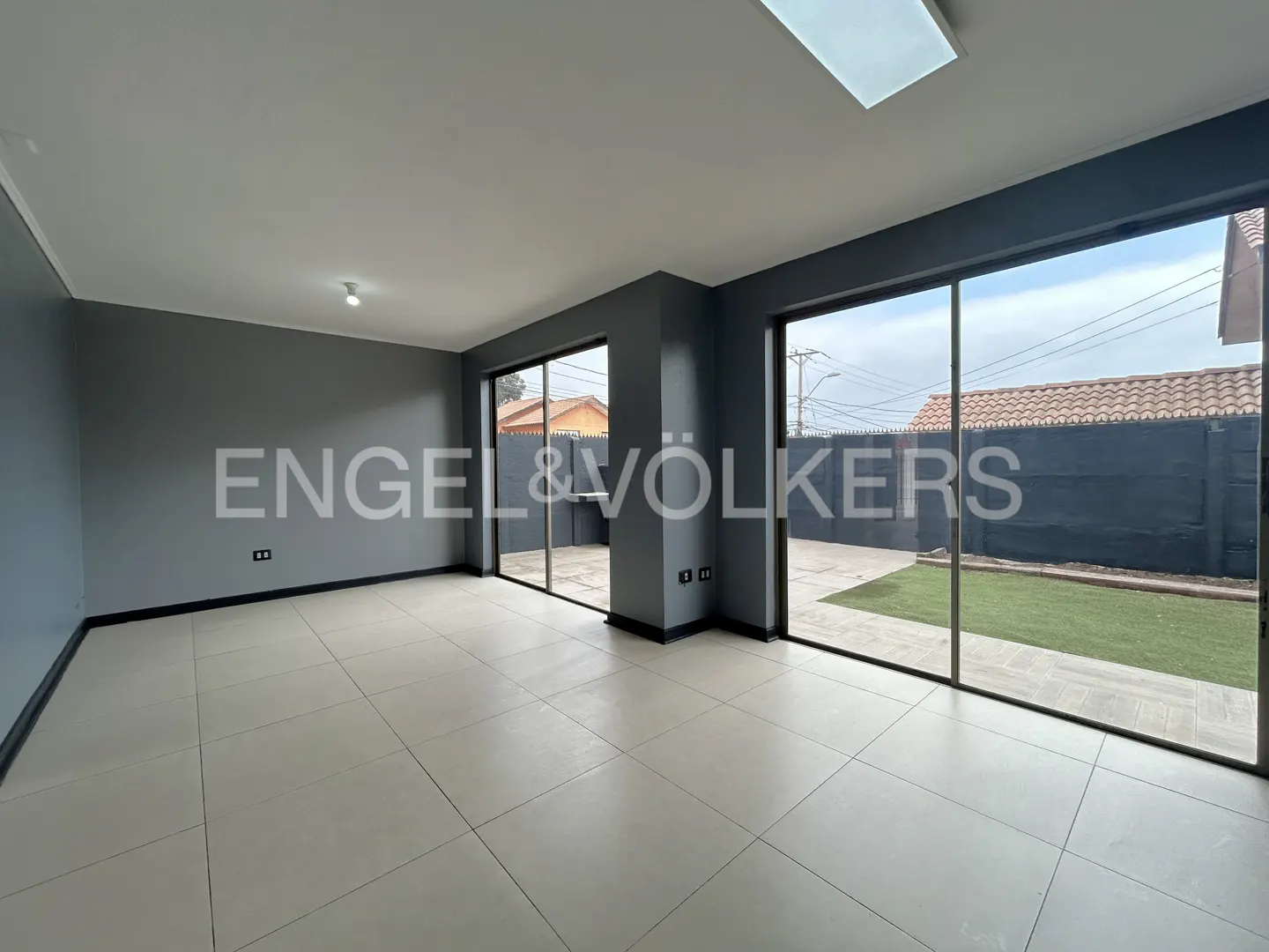 Modern living room with grey walls, light tile floors, and large sliding glass doors opening to a private backyard.