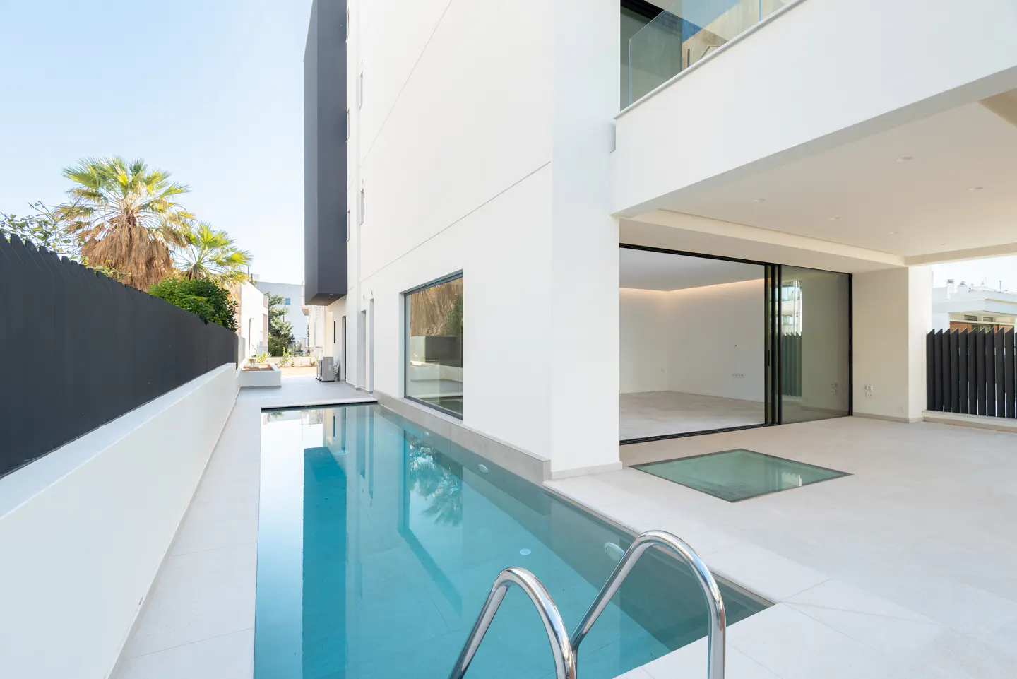 Modern white house with a blue swimming pool and metal ladder. A sliding glass door leads to an empty room.