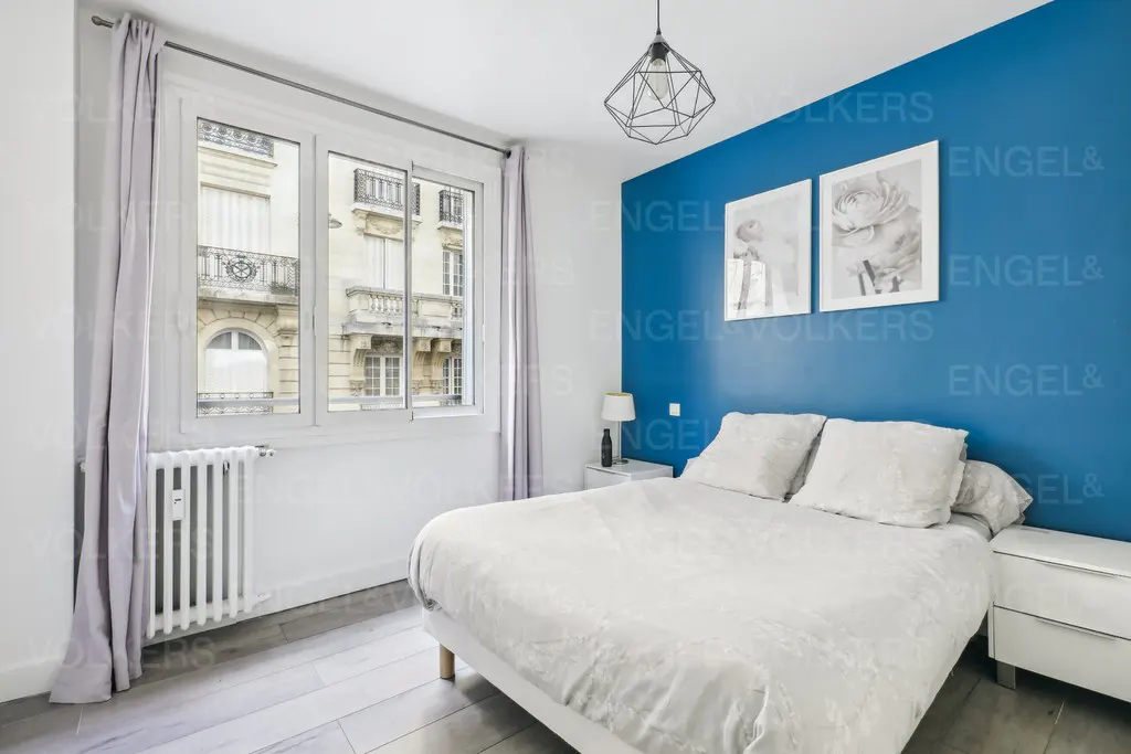 Bedroom with a white bed, blue accent wall, and a window view of a building.