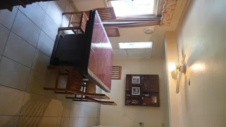 Dining room with a long, dark wood table and chairs, tile floor, and a display cabinet on the wall.