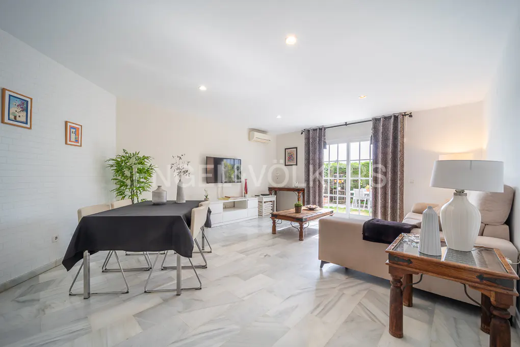 Bright living room with marble floors, dining table with black tablecloth, beige sofa, and view to the garden.