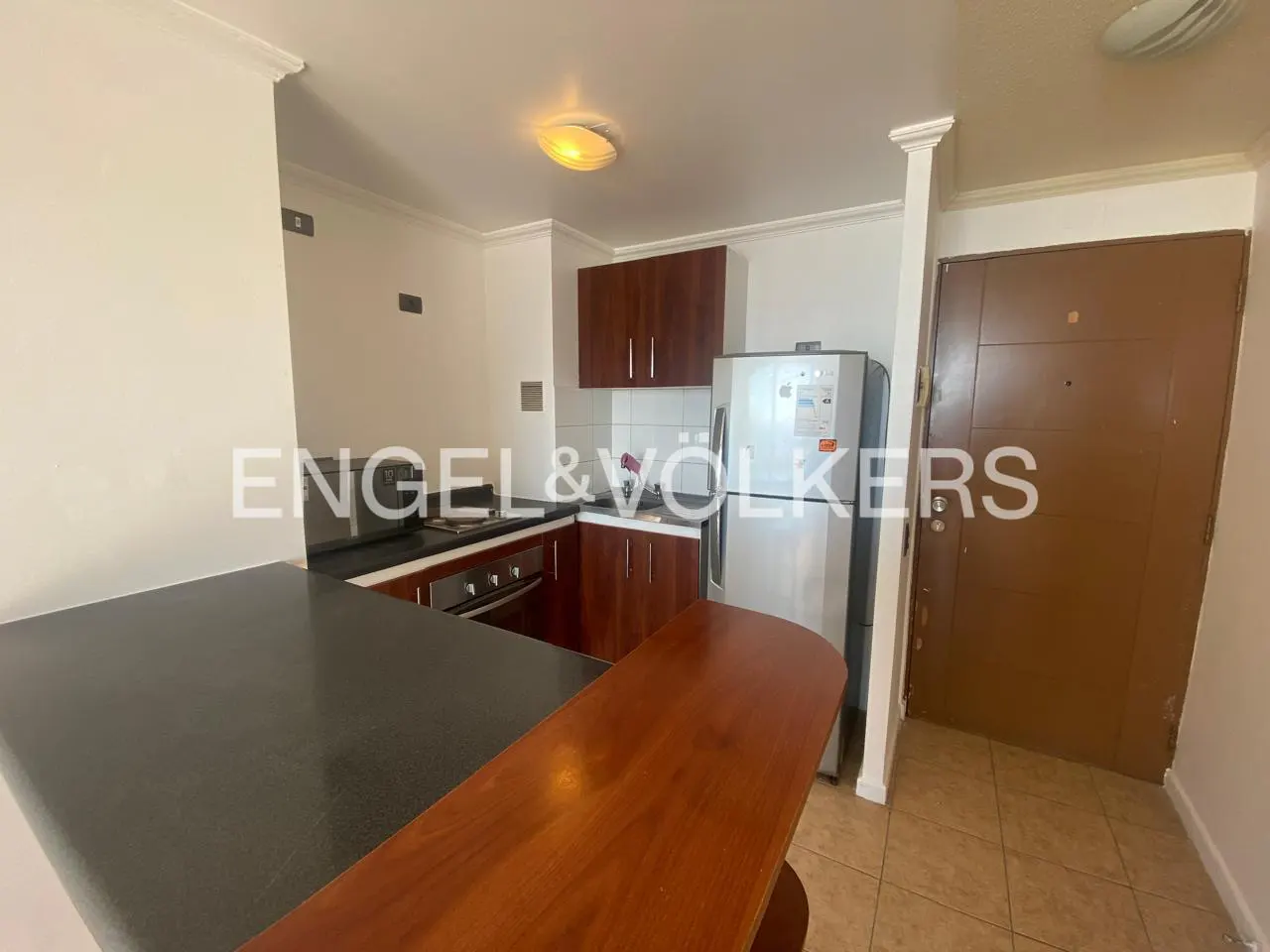 A kitchen with brown cabinets, stainless steel refrigerator, black countertop, and a brown door.